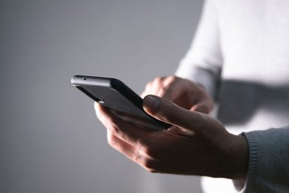 Una persona tiene in mano uno smartphone e usa il pollice per interagire con lo schermo. La scena è scarsamente illuminata, trasmettendo un'atmosfera intima e concentrata.