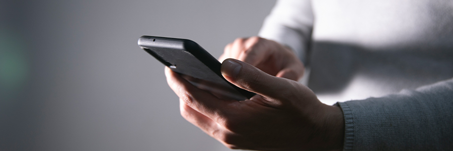 Una persona tiene in mano uno smartphone e usa il pollice per interagire con lo schermo. La scena è scarsamente illuminata, trasmettendo un'atmosfera intima e concentrata.